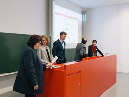 Fünf Personen stehen vor einer Tafel, Präsentation sichtbar